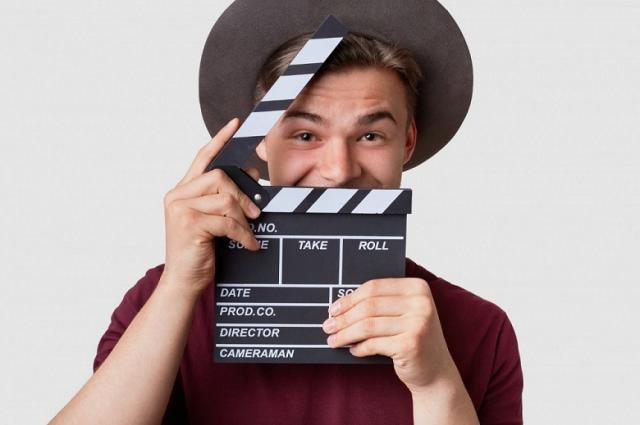 Zdjęcie przedstawia młodego filmowca trzymającego klaps fimowy