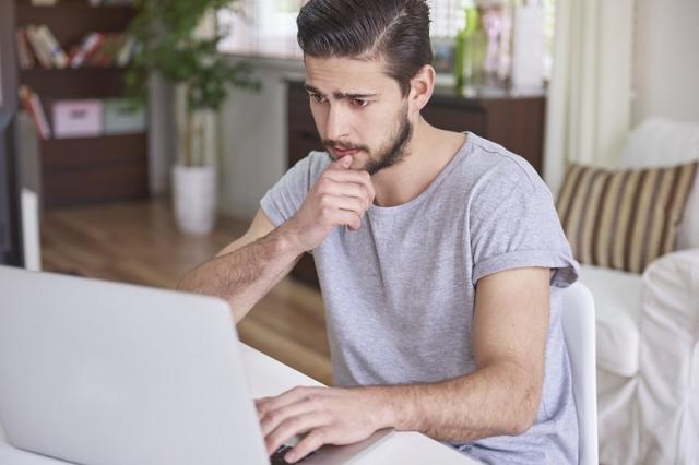 Zdjęcie przedstawia mężczyznę siedzącego przed ekranem laptopa